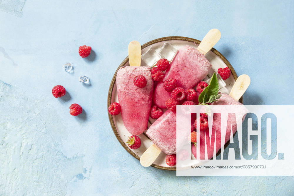 Ein Konzept für gesunde Sommergerichte: hausgemachtes Himbeereis. Vegane Himbeer-Milch-Eis am Stiel vor einem blauen Steinhintergrund. Blick von oben. Healthy summer food concept, homemade raspberry ice cream. Vegan raspberry milk popsicles on a blue stone background. View from above. (License=RF)