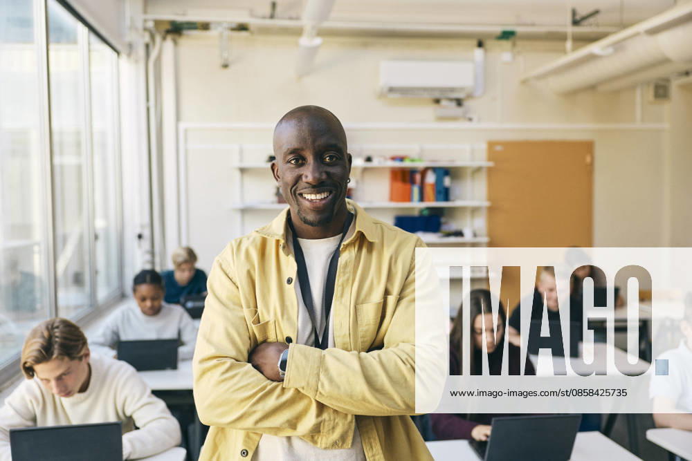 Portrait of smiling teacher standing with arms crossed in classroom at junior high school Sweden, Stockholm, model released, property released