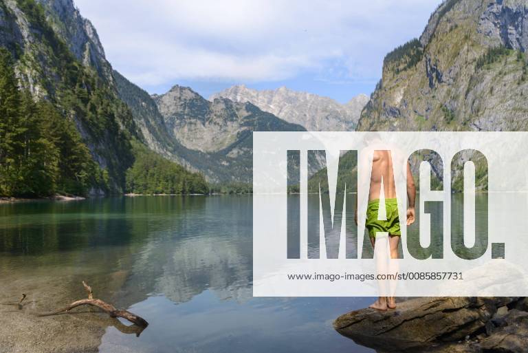Junger Mann in Badehose steht auf einem Stein im Obersee, Bergsee, Berglandschaft, hinten Watzmannmassiv, Salet am Königssee, Nationalpark Berchtesgaden, Berchtesgadener Land, Oberbayern, Bayern, Deutschland, Europa