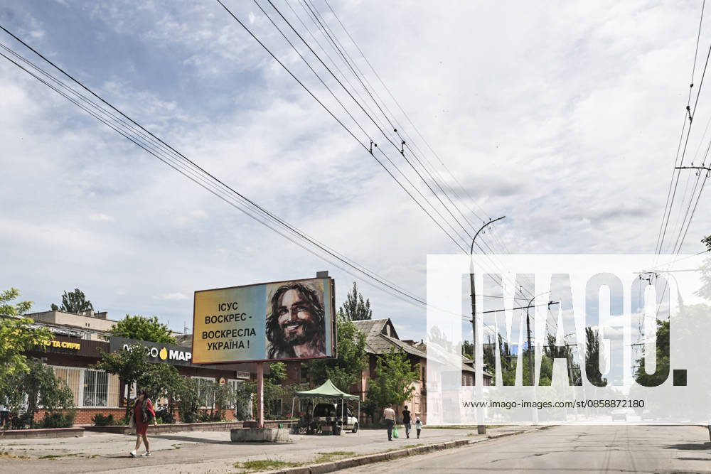 A billboard reading Jesus is risen — Ukraine will rise again stands on a street in the frontline city of Kherson, Ukraine, on June 2, 2026. The Russian army attacks the city daily with FPV drones and other unmanned aerial vehicles, deliberately terrorizing civilians. Russian forces conduct hunts for local residents, tracking them with FPV drones and dropping explosives. Police officers, medics, public transport, and urban infrastructure are also targeted. Based on the intensity of attacks, Kherson is informally divided into yellow and red zones, with the red zone considered the most dangerous due to constant shelling and drone strikes. Anti-drone netting has been installed above roads to help protect against Russian FPV drone atta