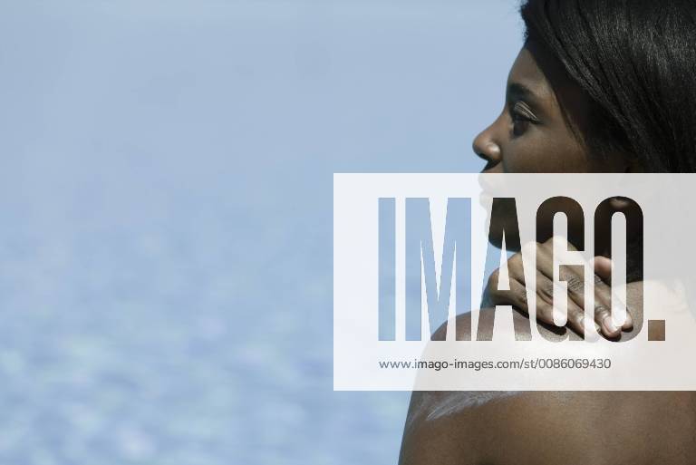 IMAGO Creative, Jahreszeit Sommer, Sonnenschutz Woman applying sunblock to shoulder, rear view