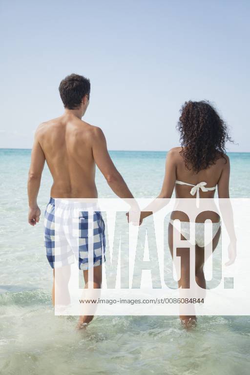 Couple holding hands while wading in sea, rear view