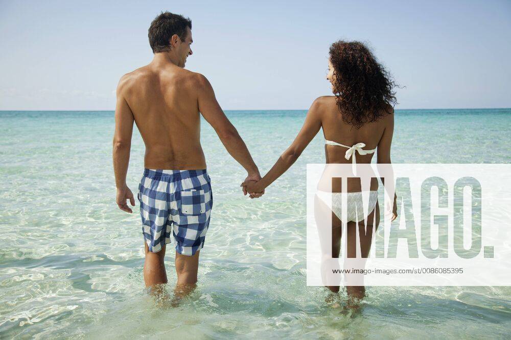 Couple holding hands while wading in sea, rear view