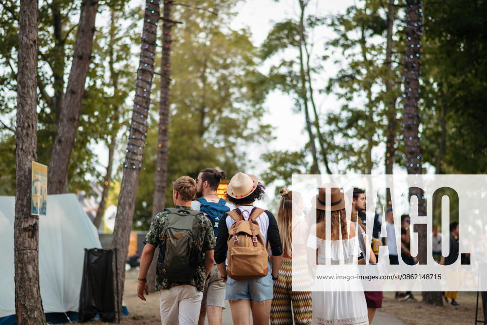 Rear view of group of young friends with backpack walking at summer festival. Rear view of group of young friends with backpack and mat walking at summer festival. model released
