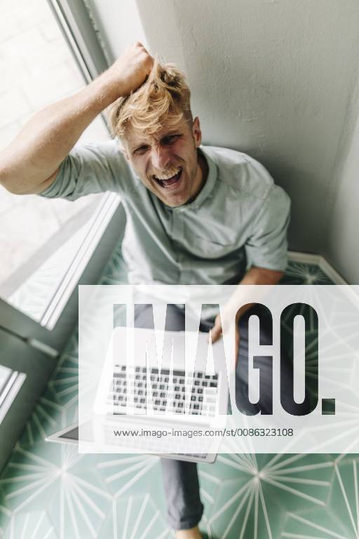 Young man sitting on ground, holding laptop, screaming in despair model released Symbolfoto property released GUSF01293