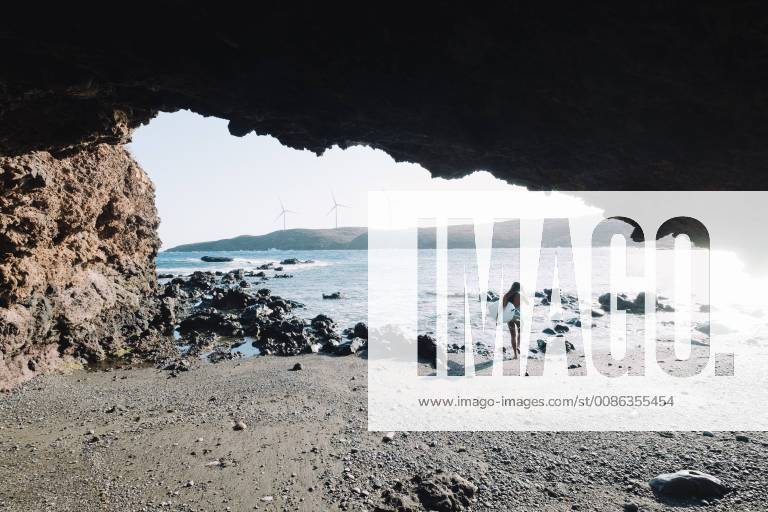 View from cave of female surfer in bikini walking with her surfboard on beach, Tenerife, Canary Islands, Spain, Tenerife Canary Islands Spain VISE004024 model released Symbolfoto