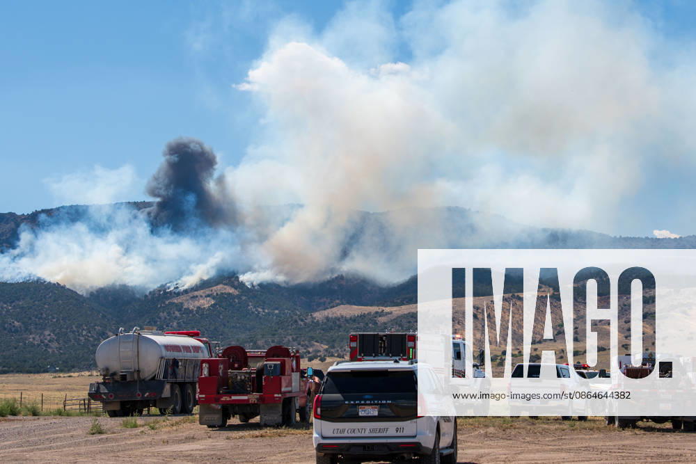 A plume of thick smoke rises into the sky above a mountain ridge as the Big Mountain Fire burns southwest of Elberta, Utah, United States, on August 23, 2026. A line of emergency response vehicles can be seen staged along a dirt road below the active wildland blaze. Elberta USA - ZUMAm292 20260823_znp_m292_004