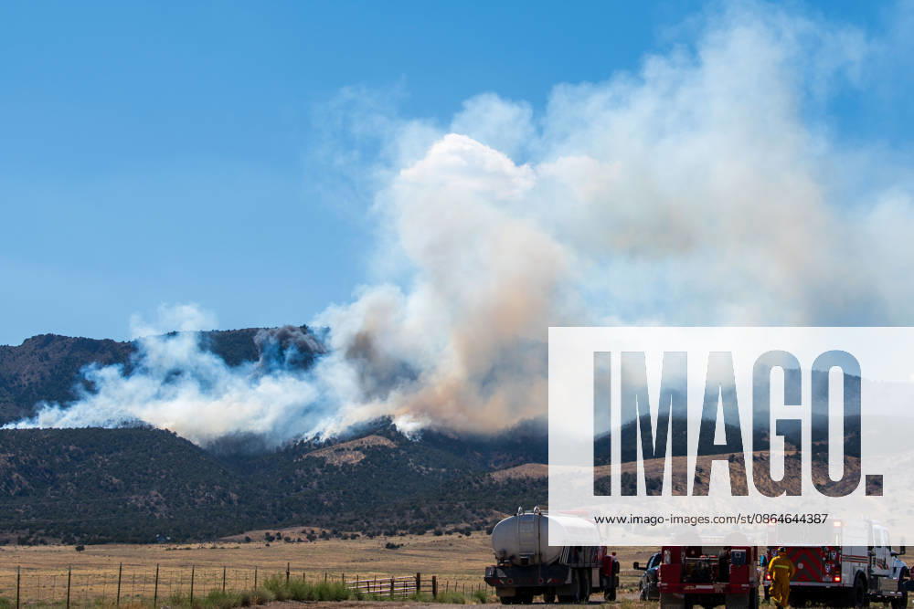 A plume of thick smoke rises into the sky above a mountain ridge as the Big Mountain Fire burns southwest of Elberta, Utah, United States, on August 23, 2026. A line of emergency response vehicles can be seen staged along a dirt road below the active wildland blaze. Elberta USA - ZUMAm292 20260823_znp_m292_005