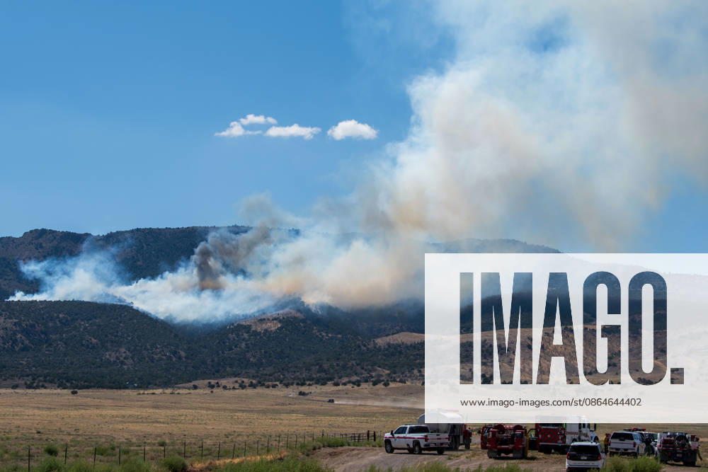 A plume of thick smoke rises into the sky above a mountain ridge as the Big Mountain Fire burns southwest of Elberta, Utah, United States, on August 23, 2026. A line of emergency response vehicles can be seen staged along a dirt road below the active wildland blaze. Elberta USA - ZUMAm292 20260823_znp_m292_008