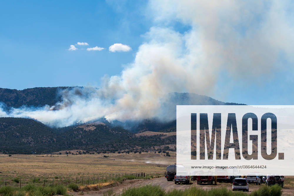 A plume of thick smoke rises into the sky above a mountain ridge as the Big Mountain Fire burns southwest of Elberta, Utah, United States, on August 23, 2026. A line of emergency response vehicles can be seen staged along a dirt road below the active wildland blaze. Elberta USA - ZUMAm292 20260823_znp_m292_009