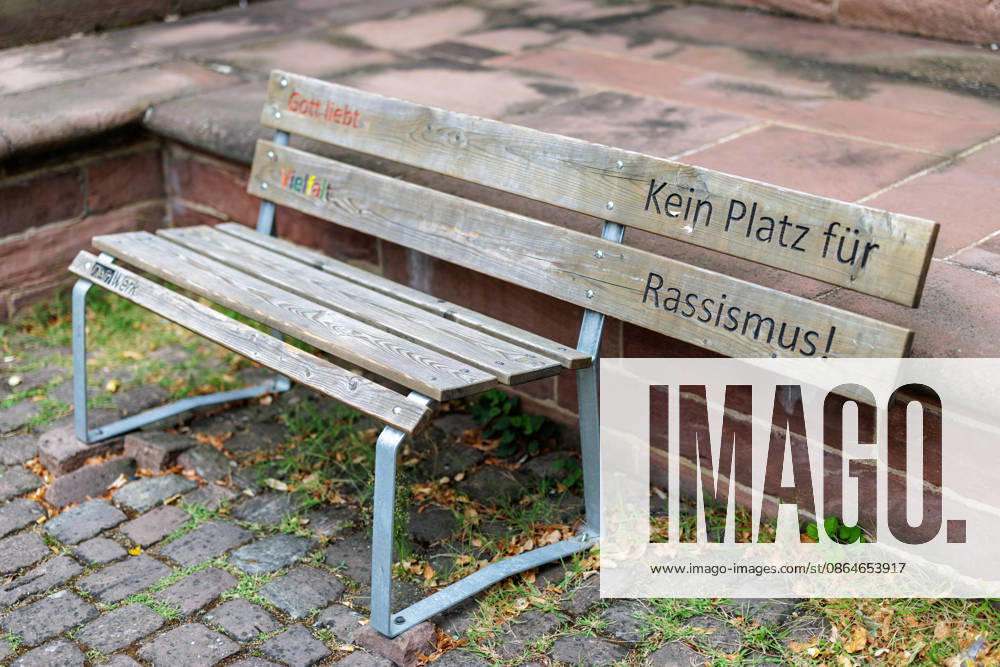 Gott liebt Vielfalt - Eine Holzbank mit den bunt eingerfrästen Schriftzügen *Gott liebt Vielfalt* und *Kein Platz für Rassismus* der Initiative *Dein Werk* steht am 17.08.2026 vor der St.-Gallus-Kirche in Ladenburg (Baden-Württemberg, Deutschland). Kirchengemeinden und christliche Initiativen setzen mit solchen gestalteteten Bänken im öffentlichen Raum sichtbare Zeichen für Toleranz, Inklusion und ein buntes Miteinander.