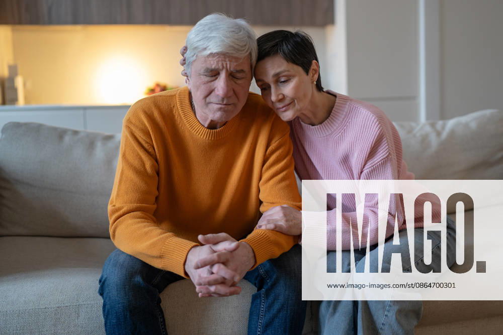 Ein älteres Ehepaar sitzt gemeinsam auf dem Sofa, umarmt sich und gibt sich in dieser schwierigen Zeit gegenseitig Halt. Elderly couple sitting on couch together embracing and supporting each other during difficult time, smiling tranquil woman hugging emotionally tired husband, loving spouse consoling partner on sofa. (License=RF) ,model released, Symbolfoto
