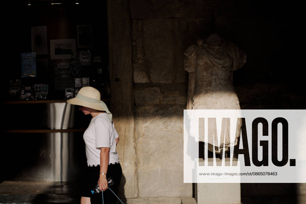 A tourist carrying a bottle of water walks past an ancient statue while visiting the Stoa of Attalos at the Ancient Agora of Athens during hot summer weather. Athens Greece - ZUMAthen 20260827_mda_x103_781