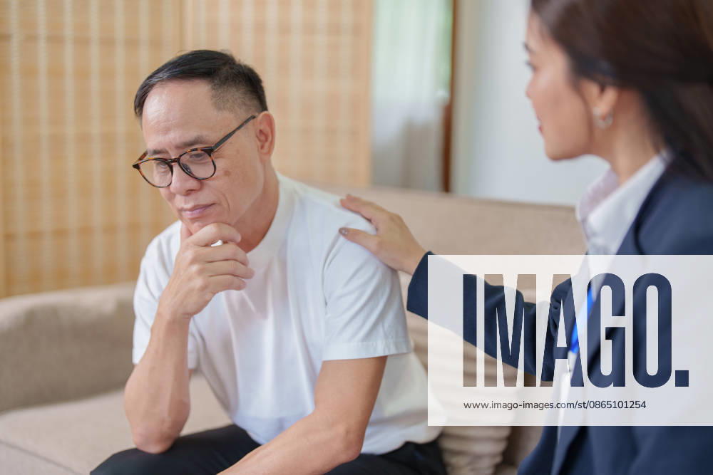 Ein Berater legt einem besorgten älteren asiatischen Mann die Hand auf die Schulter, um ihn psychisch zu unterstützen und ihm Trost zu spenden An empathetic therapist comforting a stressed Asian elderly man by placing a hand on his shoulder during a counseling session. (License=RF) ,model released, Symbolfoto