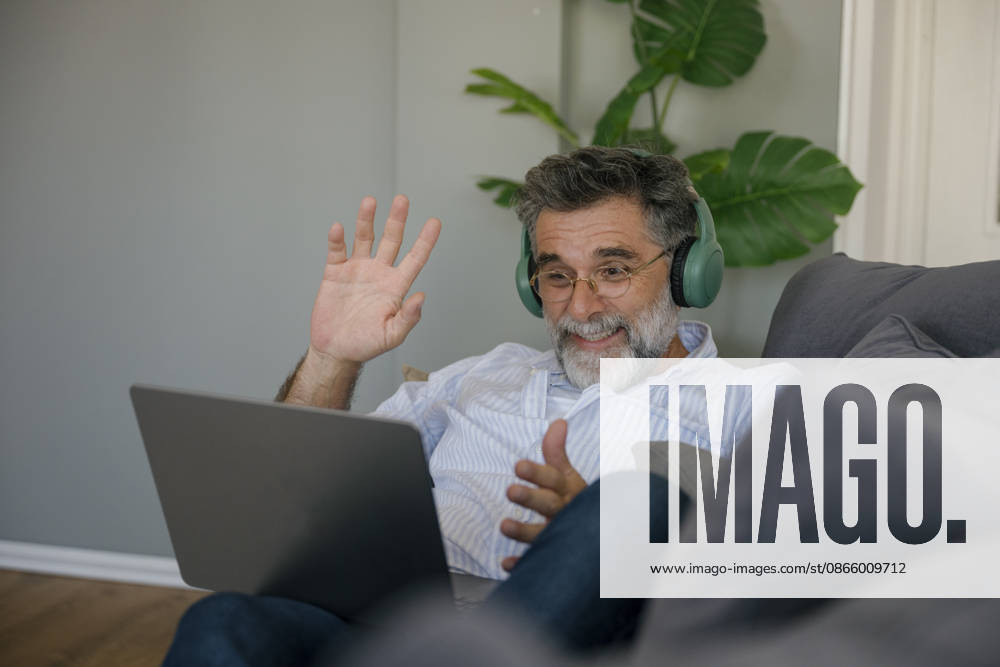 Smiling man wearing headphones using laptop for video call on couch model released, Symbolfoto property released, FLMZF02934