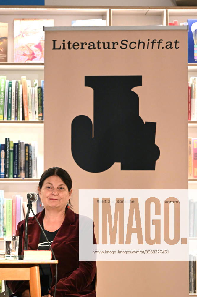 Minifestival AH0J (Literaturfestival) - Tschechien setzt über - der Kulturinitiative Literaturschiff, in der Buchhandlung Kurdirektion in Bad Ischl. Lesungen und Gespräche in Korrespondenz zum Gastauftritt Tschechiens auf der Frankfurter Buchmesse 2026. Es liest die tschechische Schriftstellerin und mehrfache Literaturpreisträgerin Radka Denemarkovich. Die Veranstaltung wrd moderiert von Julia Miesenböck, fotografiert am 30.09.26. Das Bild zei vor einem Plakat der Kulturinitiative Literaturschiffgt die Schriftstellerin Radka Denemarkovic 2026 - Minifestival AH0J (Literaturfestival) - Tschechien setzt über - der Kulturinitiative Literaturschiff, in der Buchhandlung Kurdirektion in Bad Ischl. Lesungen und Gespräche in Korrespondenz zum