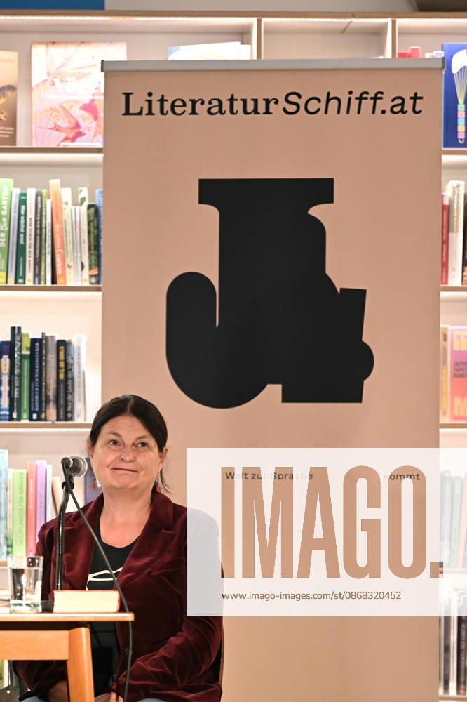 Minifestival AH0J (Literaturfestival) - Tschechien setzt über - der Kulturinitiative Literaturschiff, in der Buchhandlung Kurdirektion in Bad Ischl. Lesungen und Gespräche in Korrespondenz zum Gastauftritt Tschechiens auf der Frankfurter Buchmesse 2026. Es liest die tschechische Schriftstellerin und mehrfache Literaturpreisträgerin Radka Denemarkovich. Die Veranstaltung wrd moderiert von Julia Miesenböck, fotografiert am 30.09.26. Das Bild zei vor einem Plakat der Kulturinitiative Literaturschiffgt die Schriftstellerin Radka Denemarkovic 2026 - Minifestival AH0J (Literaturfestival) - Tschechien setzt über - der Kulturinitiative Literaturschiff, in der Buchhandlung Kurdirektion in Bad Ischl. Lesungen und Gespräche in Korrespondenz zum