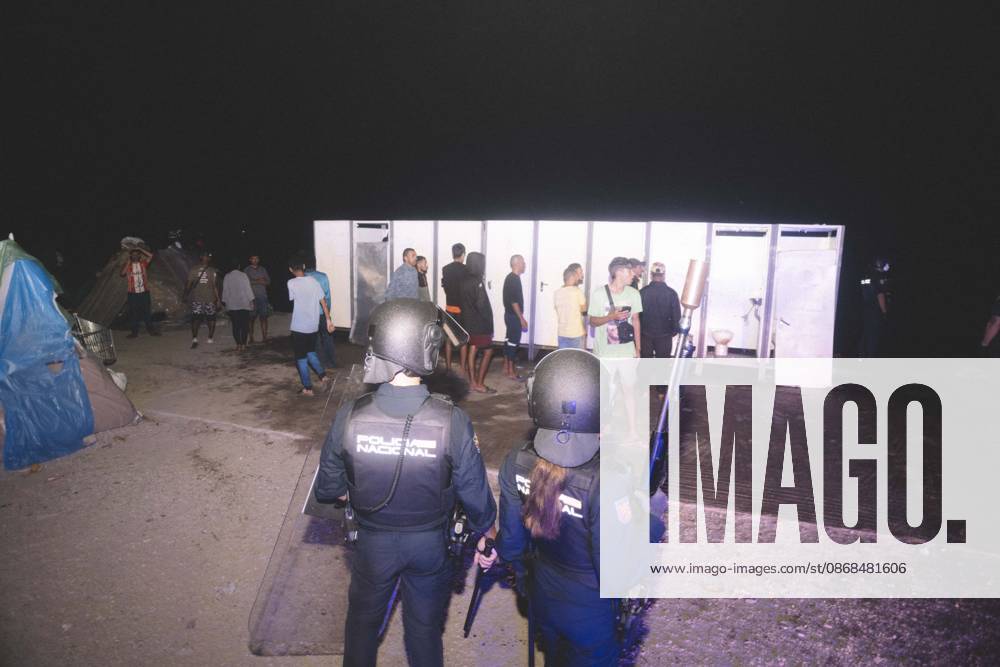 Riot police officers stand in front of the portable toilets of a makeshift migrant camp in Ceuta at night. Riot police escorted firefighters through the camp on the night of October 3 to put out the fires that people living there use to cook their food. Thousands of migrants, most of them young Moroccan men, have been living in makeshift settlements in the Spanish North African enclave of Ceuta since a mass arrival at the end of July 2026 set off a migration and political crisis. Ceuta Spain - ZUMAs392 20261003_zip_s392_005