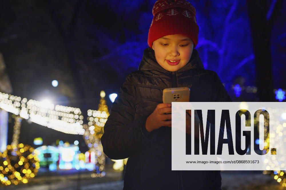 Smiling girl using smartphone outdoors at night with Christmas lights model released, Symbolfoto, AZF01532