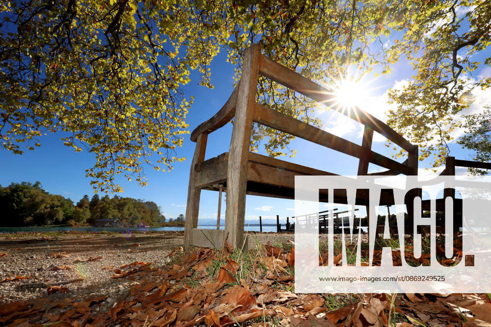 Ein Herbsttag in Feldafing, Feldafinger Park (Landkreis Starnberg). Hier der Blick auf den Starnberger See mit der Roseninsel, im Vordergrund eine Parkbank, Sitzbank, die Sonne, Sonnenstrahlen blinzeln durch die Blätter, gefärbte Bäume, Laubfärbung, Laubbaum, herbstlich, Farbenspiel, Herbstlaub, Herbstfärbung, Blattfärbung, rot, gelb, rotes Laub, gelbes Laub, Naturschauspiel, Herbstbild, Herbstimpression, Wetterbild, goldener Oktober
