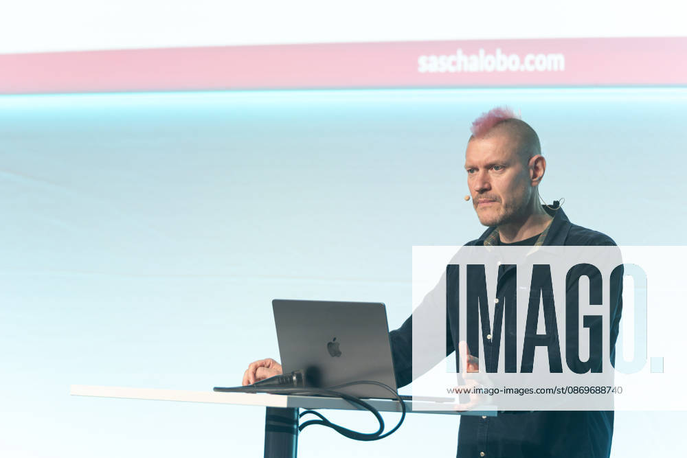 Berlin, 16.10.2026: Auf der NeulandPro Connect 2026 spricht der Publizist und Digital-Vordenker Sascha Lobo am Rednerpult zum Publikum. Die zweitägige KI-Konferenz NeulandPro Connect 2026 findet am 16. und 17. Oktober im Westhafen Event & Convention Center (WECC) in Moabit statt, einem historischen Speichergebäude am Berliner Westhafen. Veranstalter ist NeulandPro, eine Bildungs- und Medienmarke rund um Künstliche Intelligenz. Mit Vorträgen, Workshops und Hackathons richtet sich die Konferenz vor allem an kleine und mittelständische Unternehmen, Gründer und Führungskräfte, die KI praktisch einsetzen wollen; erwartet werden bis zu 1.000 Gäste. NeulandPro Connect 2026 - KI-Konferenz in Berlin