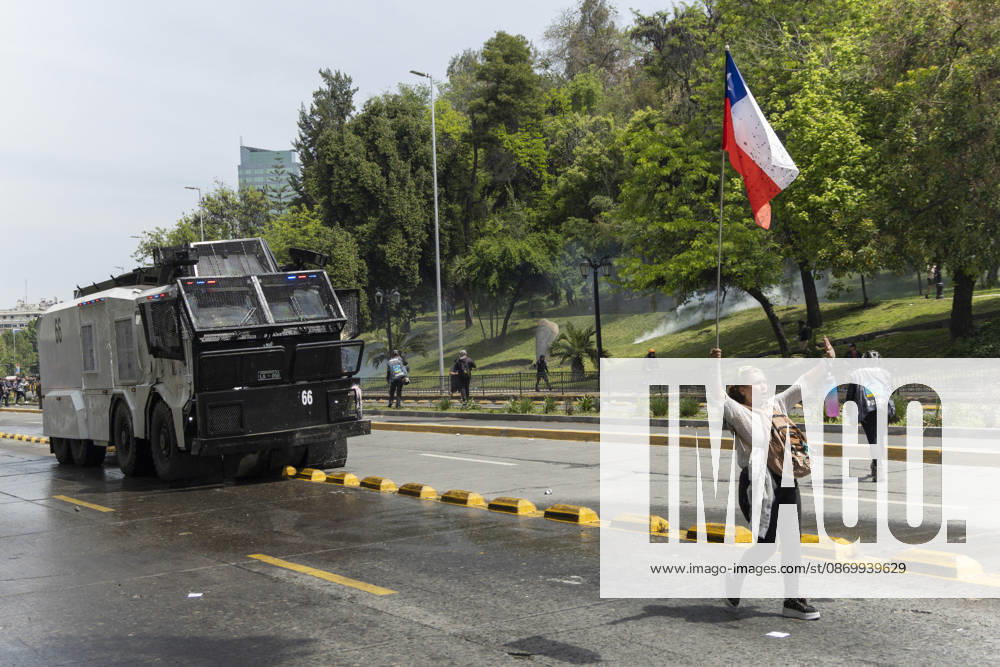 A woman walks with a Chilean flag in front of an armored police car. In the center of the capital of Chile, different incidents took place between demonstrators and the police. The riots were carried out during the commemoration of the 7 years after the social outcast that happened on October 18, 2019. Santiago Chile - ZUMAs197 20261019_aaa_s197_016