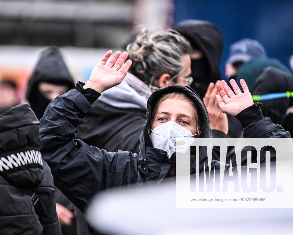 A young blonde woman wearing a black hood and a face mask raises both hands conspicuously during a student protest in central Brussels, Belgium, on 24 October 2026. The gesture takes place amid demonstrations and repeated police interventions in the city centre.