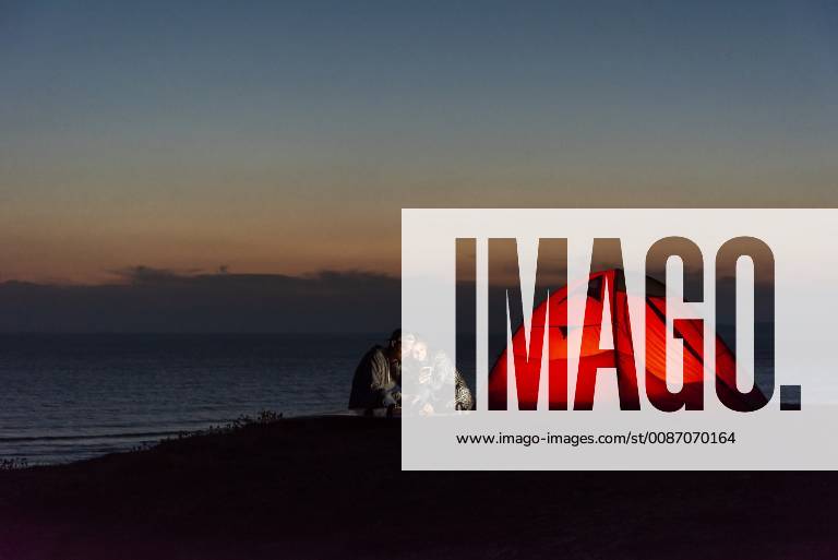 IMAGO Creative: Klimawandel - Nachhaltiges Reisen Romantic couple camping on the beach, using smartphone model released Symbolfoto UUF15172
