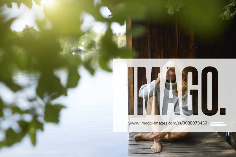 IMAGO Creative, Sommer, Schatten-Plätze bei Hitze Smiling relaxed woman sitting on wooden jetty at a remote lake model released Symbolfoto PNEF01047
