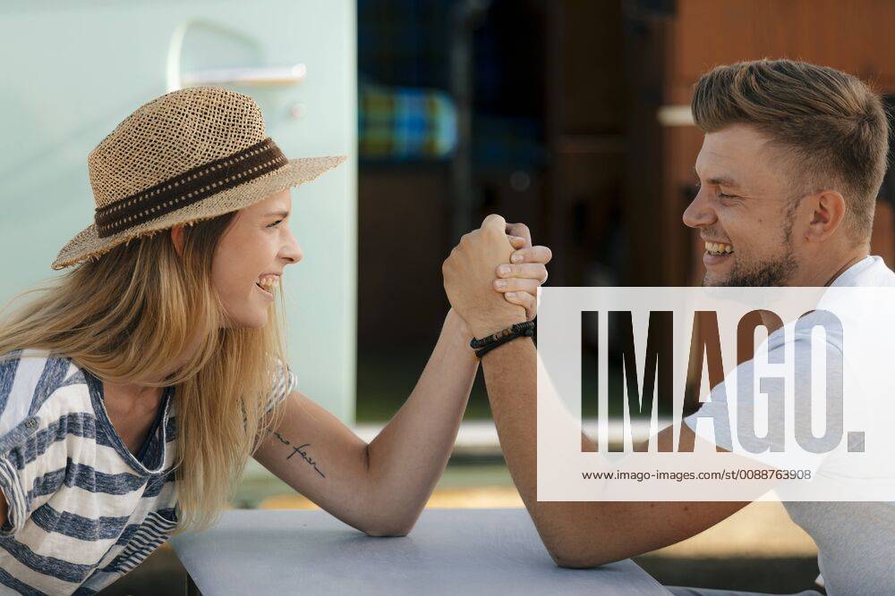 Happy young couple armwrestling at camper van model released Symbolfoto GUSF01579