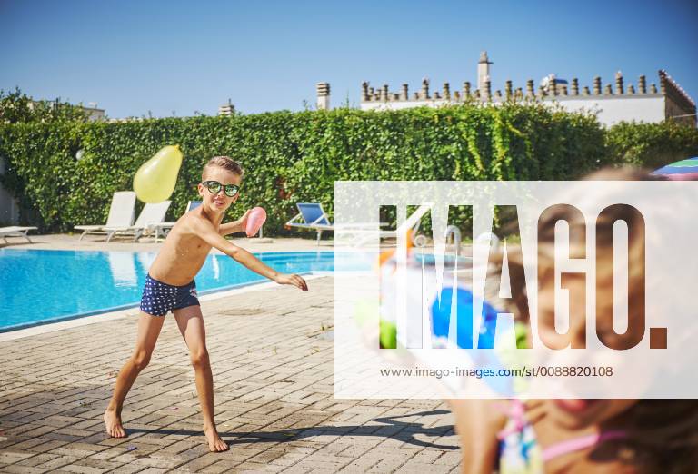 Girl and boy having a water fight with water gun and water bombs at the poolside model released Symbolfoto DIKF00311