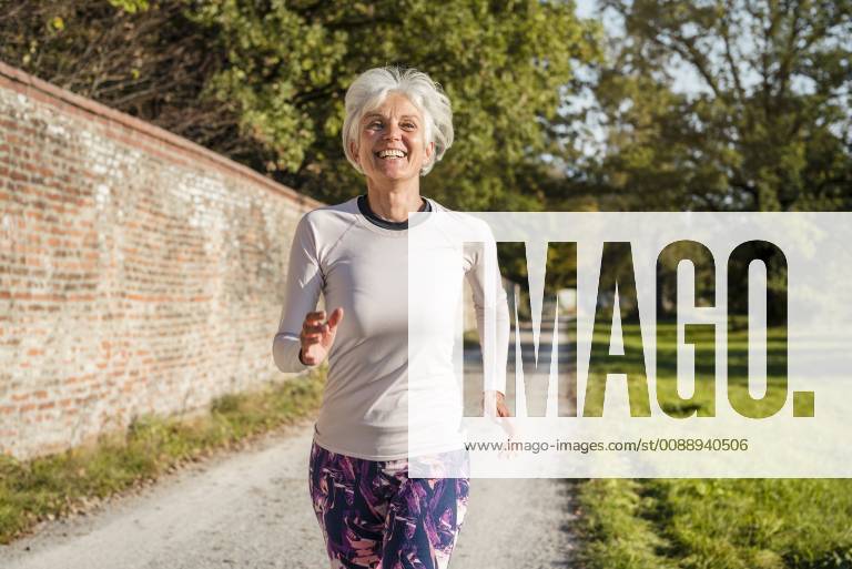 Happy senior woman running along brick wall in a park model released Symbolfoto DIGF05436