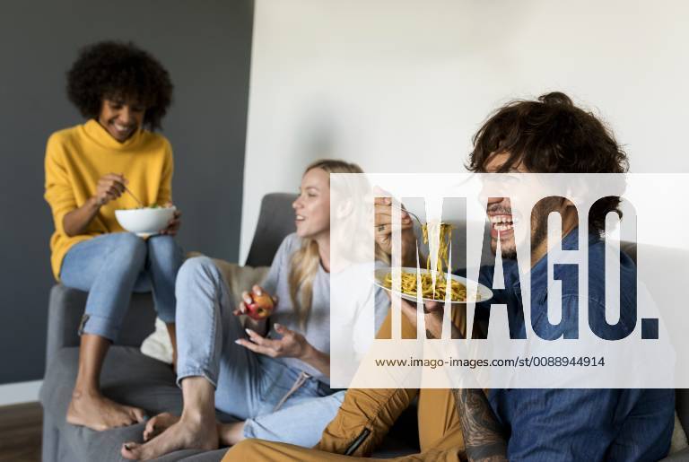 IMAGO Creative, Lifestyle, Leben in einer Wohngemeinschaft, WG Cheerful friends sitting on couch talking and eating model released Symbolfoto property released VABF01887