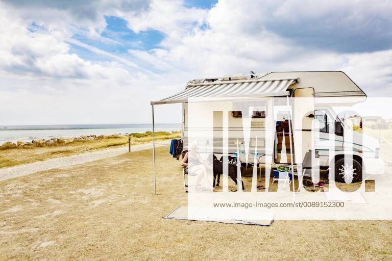 Frau sitzt im Urlaub mit einem Hund, Königspudel vor ihrem Wohnmobil am Meer, Portbail, Normandie, Frankreich, Europa