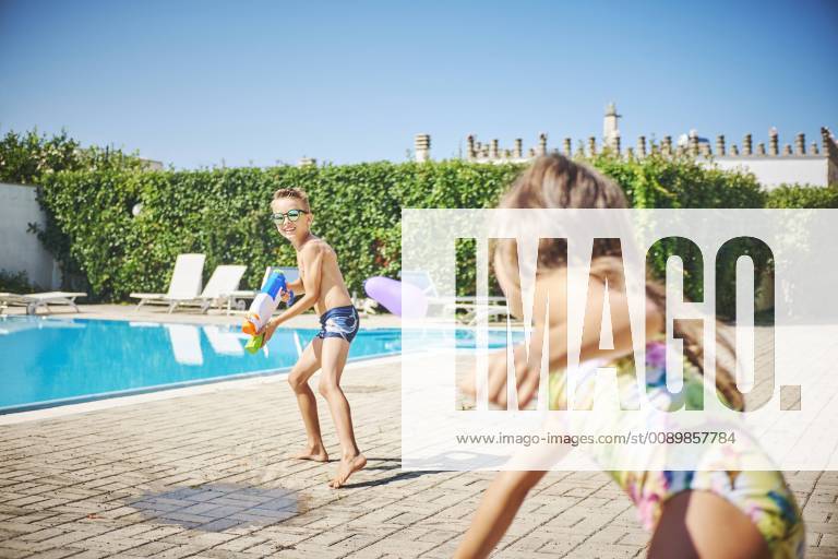 Girl and boy having a water fight with water gun and water bombs at the poolside model released Symbolfoto DIKF00307