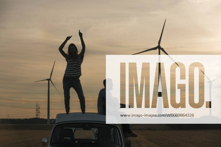 IMAGO Creative: Ende des Sommers Happy couple with guitar on roof of a camper van in rural landscape at dusk model released Symbolfoto GUSF01553