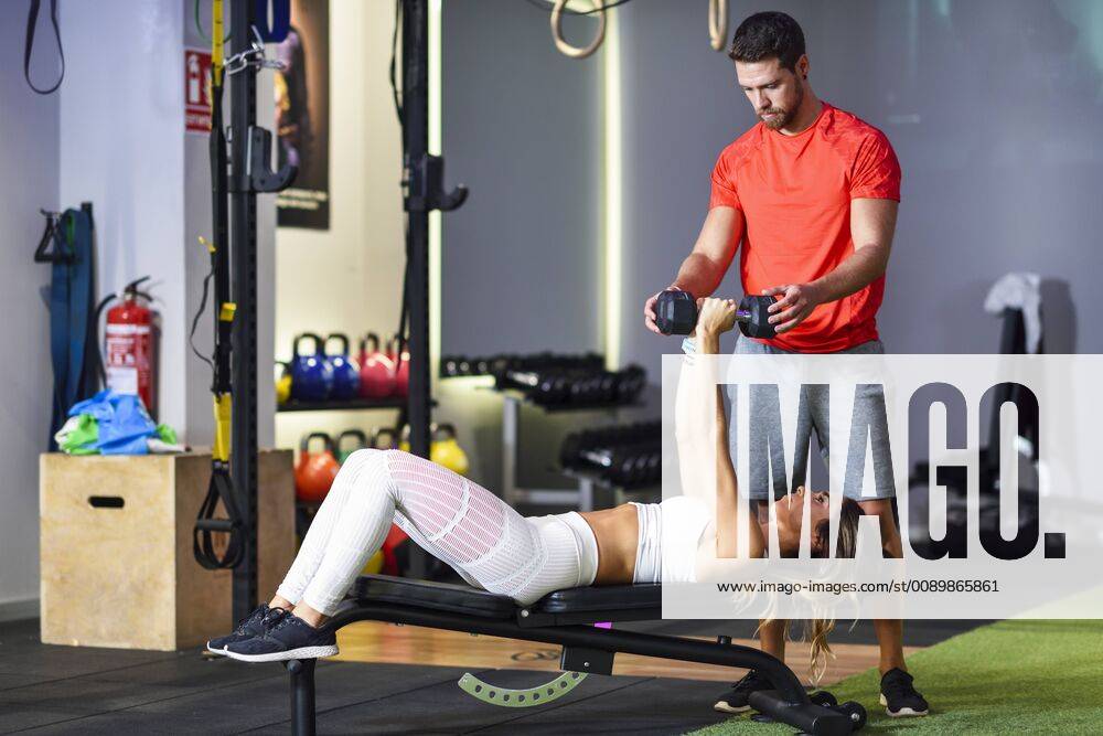 Personal trainer assisting client with weight training, lifting dumbells, lying on bench model released Symbolfoto property released JSMF00493