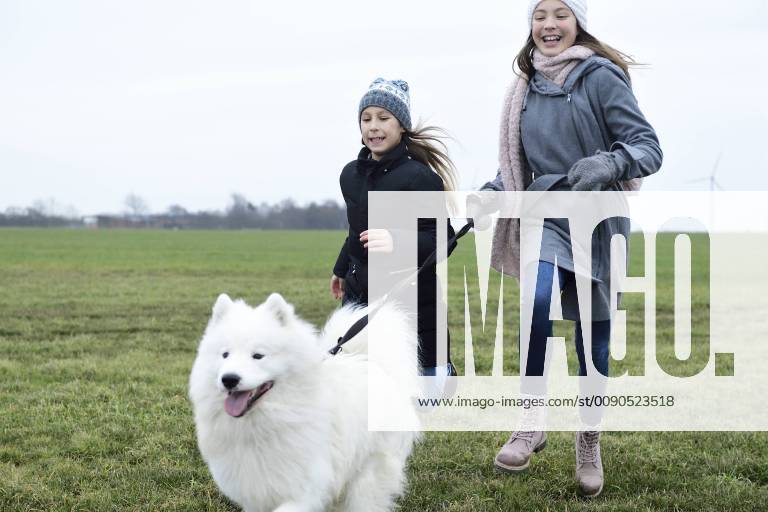 Two girls running on a meadow with dog having fun model released Symbolfoto property released ECPF00259