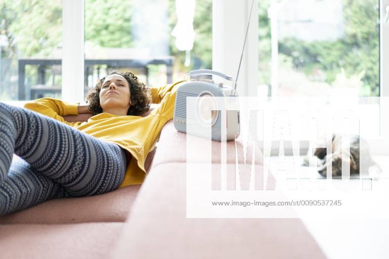 Woman lying on couch listening to music with portable radio at home model released Symbolfoto property released JOSF02698