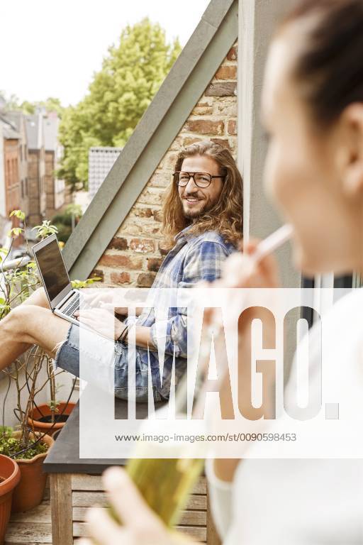 Young couple sitting on their balcony in summer, man using laptop model released Symbolfoto property released PESF01101