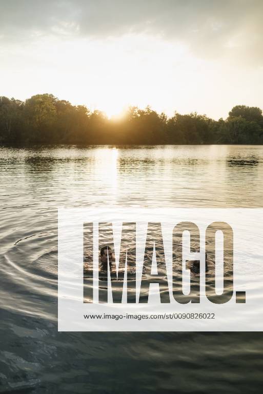 Old and young man swimming in a lake at sunset model released Symbolfoto GUSF01825