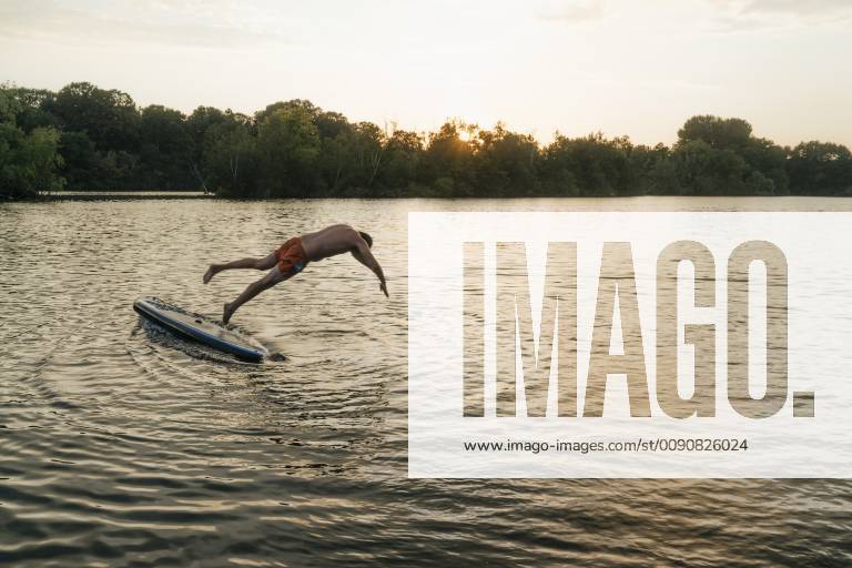 Man jumping from SUP board on a lake at sunset model released Symbolfoto GUSF01827