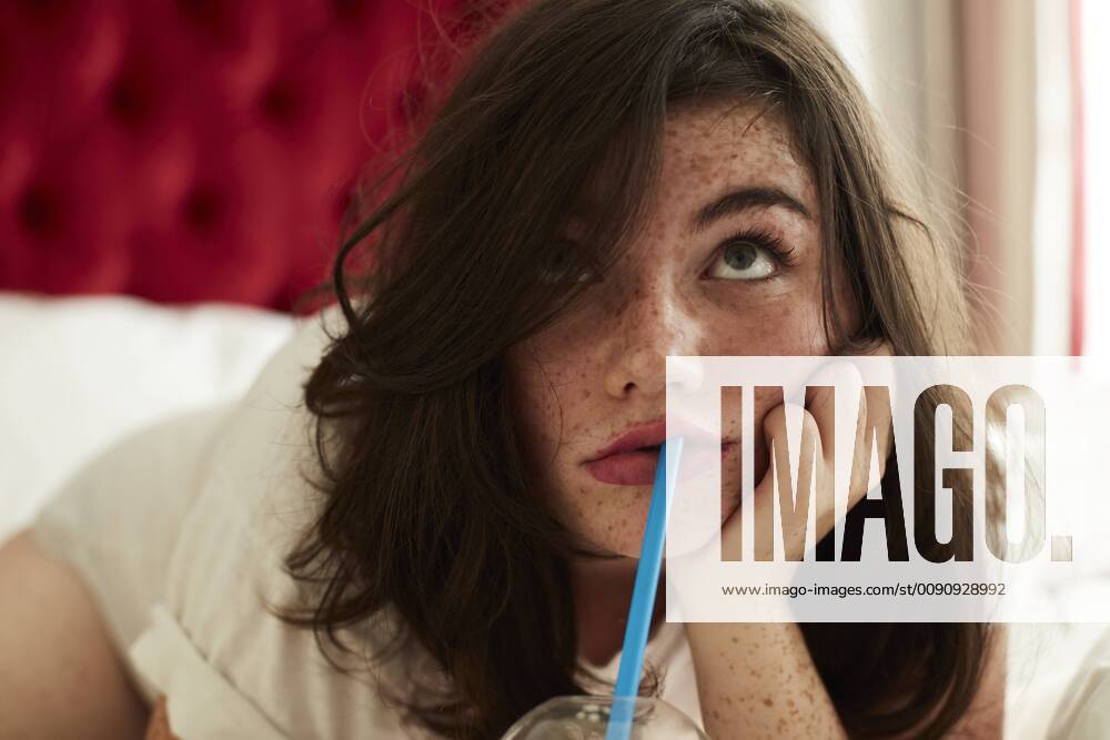 Portrait of bored teenage girl lying in bed with soft drink model released Symbolfoto AMEF00019