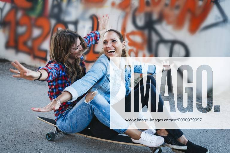 Two laughing friends sitting on longboard with arms outstretched model released Symbolfoto HMEF00251