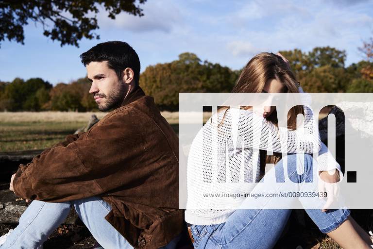 Serious couple sitting back to back in a park model released Symbolfoto IGGF00835