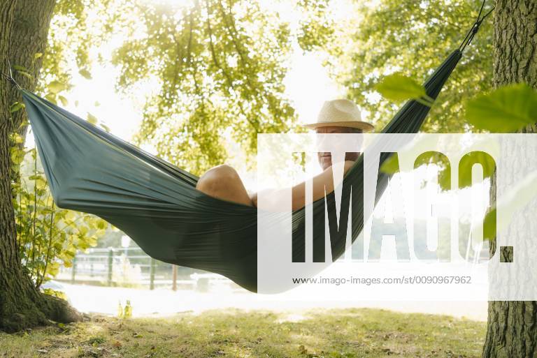 Senior man wearing straw hat relaxing in hammock at lakeshore model released Symbolfoto property released GUSF01783