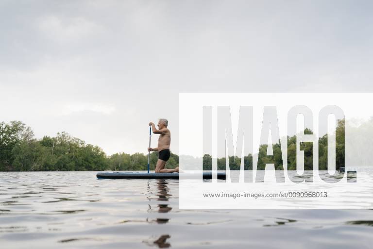 Senior man kneeling on SUP board model released Symbolfoto GUSF01797