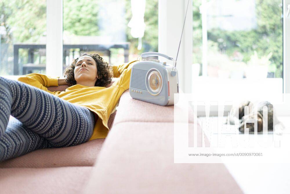 Woman lying on couch listening to music with portable radio at home model released Symbolfoto property released JOSF02698