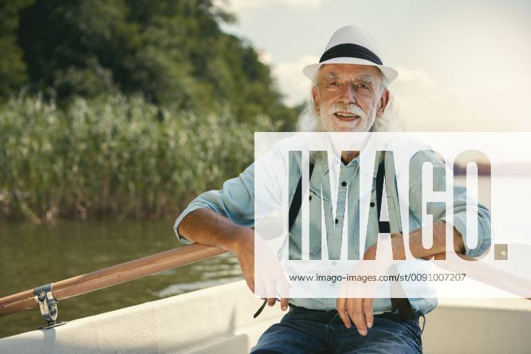 Portrait of senior man sitting in rowing boat on a lake wearing suspenders and summer hat model released Symbolfoto VWF00018