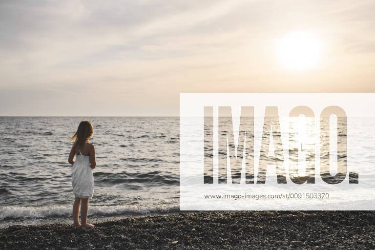 Little girl in white dress looking at sunset over the sea model released Symbolfoto EYAF00116